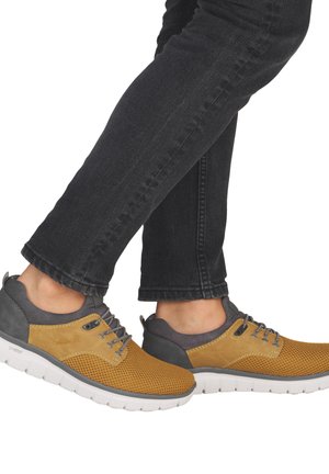 Chaussures de sport dotées d'une tige en mesh jaune respirant, d'accents gris et d'une semelle blanche amortie. Lacets détaillés et améliorations de texture.