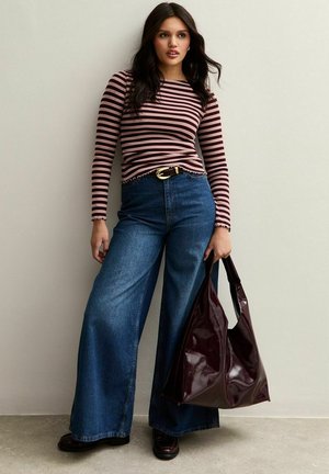 Lange mouw gestreepte top in roze en donkerbruin, hoogwaisted wijde denim jeans, en een glanzende bordeauxrode tote tas, gedragen met donkere schoenen.