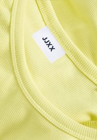 Tecido amarelo estriado com uma textura suave, apresentando um decote redondo e uma etiqueta branca com a inscrição "JJXX" costurada dentro.