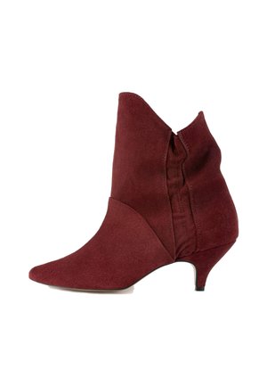 Burgunderfarvet ruskindsankelstøvle med spidse tæer, asymmetrisk design og lav hæl. Har en sidesøm for fleksibel pasform.