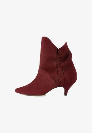 Burgunderfarvet ruskindsankelstøvle med spidse tæer, asymmetrisk design og lav hæl. Har en sidesøm for fleksibel pasform.