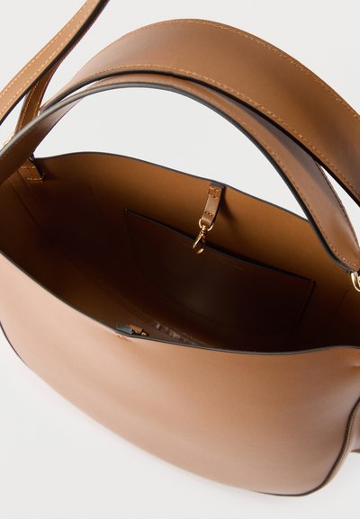 Τσάντα από δέρμα σε ταμπά χρώμα με φαρδιά λουρίδα, ανοιχτό επάνω μέρος, εσωτερική τσέπη και μικρό χρυσό κούμπωμα στο εσωτερικό, σε απλό φόντο.