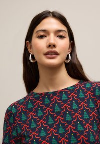 Chemise marine avec un motif répété de sapins de Noël verts et de nœuds rouges, avec un col rond et des manches courtes, fabriquée en tissu doux.