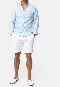 Camisa de botones a rayas azul claro en tela suave, combinada con pantalones cortos de lino blanco y alpargatas blancas, con las mangas remangadas.