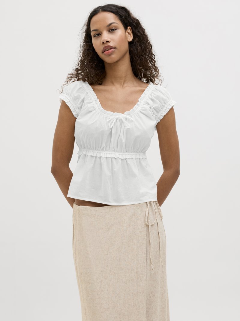 Witte katoenen top met een vierkante halslijn, ruches aan de mouwen en een gathered taille. Gecombineerd met een beige, lichtgewicht, trekkoordrok.