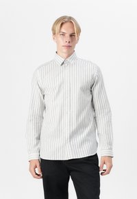 Camicia a maniche lunghe con bottoni di colore beige chiaro con sottili righe verticali. Il tessuto è liscio, con colletto classico e chiusura a bottoni.