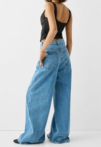 Szerokie dżinsy z niebieskiego denimu z wyblakłym efektem, wysokim stanem i dwoma tylnymi kieszeniami. Połączone z dopasowanym czarnym topem na ramiączkach.