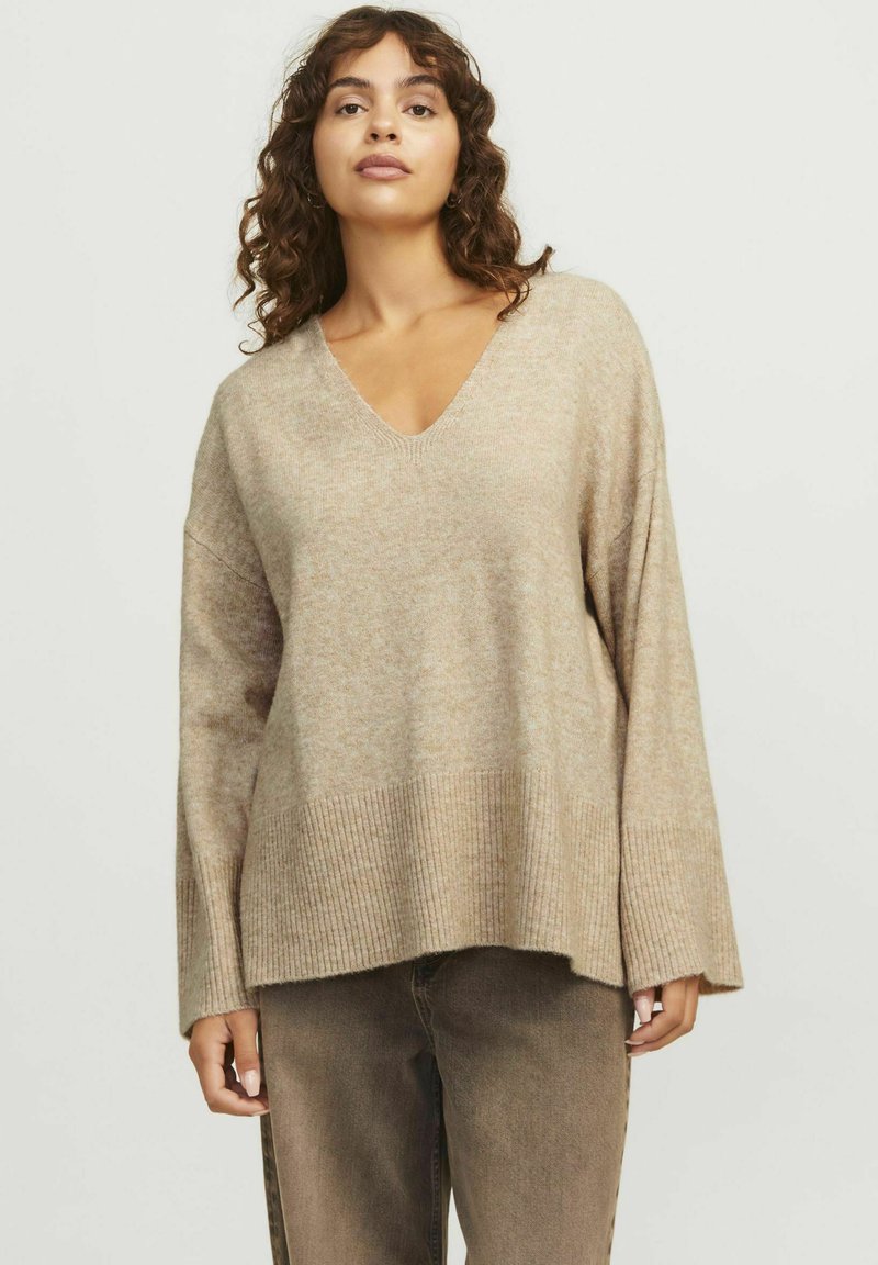 Beige v-ringad tröja med långa ärmar och ribbad nederdel. Mjuk textur, avslappnad passform och har en något oversized design. Kombination med bruna byxor.