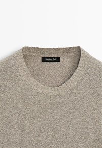 Beige strikket sweater med rund hals og ribbet krave, mærket "Massimo Dutti, Made in Romania," vist på en hvid baggrund.