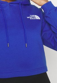 Felpa blu corta in cotone, con cappuccio regolabile dotato di occhiali argentati e un logo bianco. Tessuto strutturato con polsini a coste.