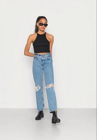 Top cropped preto com alças, jeans de cintura alta azul claro com detalhes desgastados e botas de tornozelo pretas chunky. Os acessórios incluem óculos de sol.