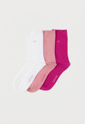 Tre par bomuldssokker: hvide, lyserøde og fuchsiafarvede. Hver har en logo med pink tekst nær manchetterne. Glat tekstur, ankel-længde design.