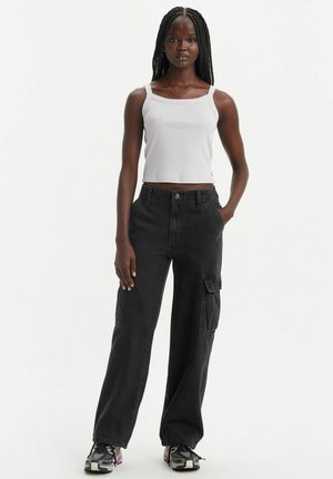 Black cargo pants with side pockets, paired with a white ribbed tank top. The outfit features a relaxed fit and subtle stitching details.