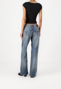 Blå vida jeans med blekt tvätt, fem fickor och en brun läderlogotyp på midjan. Svart ribbat linne med korta ärmar.