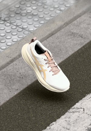 Chaussure de course blanche et rose clair suspendue au-dessus d'un trottoir texturé et d'une rue en asphalte près du bord et du revêtement tactile.
