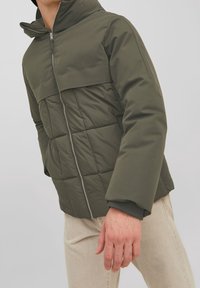 Giacca a vento color verde oliva con cappuccio, dotata di zip frontale, design trapuntato e polsini a contrasto. Tessuto morbido e liscio al tatto.