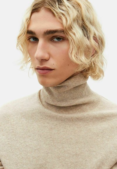 Maglione a collo alto beige in morbido knit a coste. Dettaglio ravvicinato sulla texture del tessuto con una finitura liscia, caratterizzato da un collo aderente e un motivo sottile.