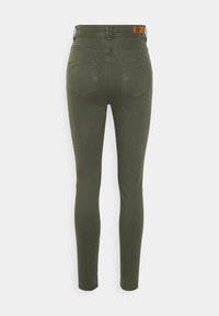 Pantalon slim kaki avec poches arrière et patch de marque en cuir sur la ceinture, vu de dos sur fond blanc.