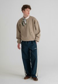 Beige oversized sweatshirt with ribbed cuffs, paired with dark blue pants featuring cream side stripes; model wearing a patterned scarf.
