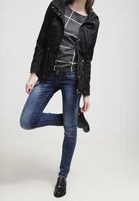 Czarna kurtka z kapturem na szarej koszuli w paski z długim rękawem, zestawiona z niebieskimi dżinsami i czarnymi botkami za kostkę. Gładka tkanina i dopasowany krój.