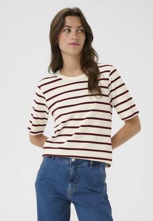 T-shirt rayé crème avec des bandes horizontales bordeaux. Manches courtes, col rond, coupe décontractée. Associé à un jean en denim bleu.
