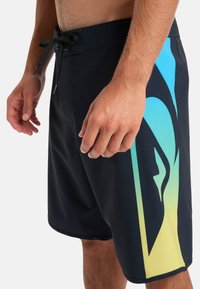 Schwarze Boardshorts aus leichtem Material; mit einem Verlauf von Blau nach Gelb auf der Seite und einem Kordelzugbund.