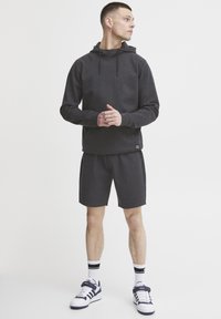 Mørkegrå hettegenser med hette, kombinert med matchende shorts. Har myk stoff og sidestreker. Bært med hvite og marineblå sneakers.