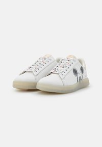 White sneakers featuring a textured sole, lace-up design, and graphic Mickey Mouse accents on the outer sides. Colorful printed laces.