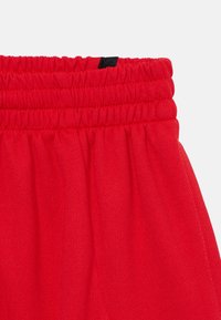 Shorts de sport rouges avec une taille élastique, dotés d'un tissu texturé froncé et d'un accent en étiquette noire près du haut.