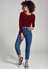 Crop top a strisce rosse e nere con maniche lunghe, jeans in denim blu a vita alta e sneakers in tela nere con dettagli bianchi.