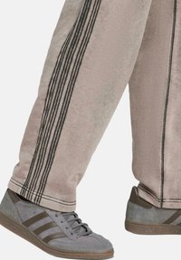 Ljust rosa mjukisbyxor med mörka vertikala ränder, kombinerat med grå sneakers som har tre mörka ränder och strukturerade detaljer på sulan.