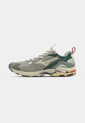 Zapatilla deportiva en tonos gris y verde con parte superior texturizada, suela acolchada y acentos rojos en contraste. Presenta un logo reflectante en el lateral.