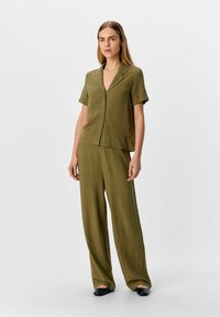 Blouse boutonnée à manches courtes en vert olive, assortie à un pantalon large. Tissu lisse et léger avec une coupe décontractée.