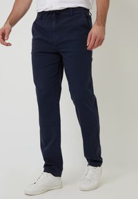 Chinos azul marino con un diseño de pierna recta, hechos de tela de algodón, con cintura elástica y bolsillos laterales, combinados con zapatillas blancas.