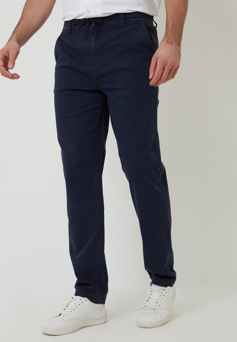 Chinos azul marino con un diseño de pierna recta, hechos de tela de algodón, con cintura elástica y bolsillos laterales, combinados con zapatillas blancas.
