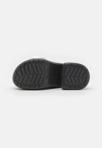 Black rubber shoe sole with textured pattern, featuring deep grooves and ridges for traction. Includes logo imprint in the center.