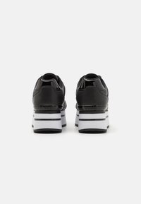 Schwarze Sneaker mit glänzenden Akzenten, ausgestattet mit einer klobigen, weiß-schwarz gestreiften Sohle, abgerundetem Absatz und strukturiertem Obermaterial.