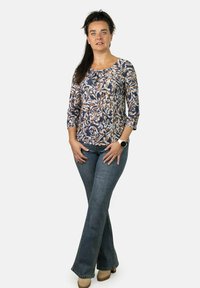 Blusa con estampado floral en colores azul, crema y óxido, con mangas de tres cuartos, combinada con jeans de campana de mezclilla y zapatos de tacón color tostado.