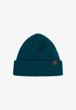 Teal gebreide beanie met een omgeslagen rand. Heeft een geribbelde textuur en een label dat aan de zijkant is genaaid met de tekst "PROTEST HOUSE OF SNOW."