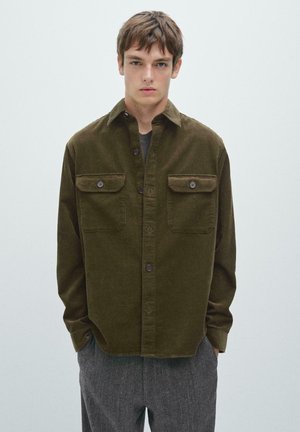 Chemise en velours côtelé vert olive avec deux poches poitrine et fermetures à bouton. Conçue avec un col classique et une coupe décontractée.