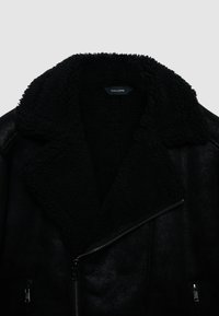 Giacca nera in ecopelle con ampio colletto in shearling testurizzato, chiusura con zip inclinata e due tasche frontali con zip. La fodera è morbida e pelosa.