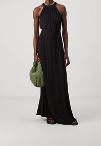 Mustapuku, jossa on solmittava vyötärö, sileä kangas ja korkea kaula-aukko. Yhdistetty teksturoidun vihreän laukun ja mustien sandaalien kanssa.