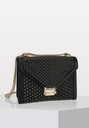 Zwarte leren handtas met een doorgestikt chevronpatroon, gouden studs, een gouden kettingriem en een opvallende metalen sluiting.