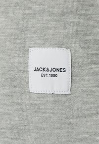 Tissu gris avec une texture douce présentant une étiquette blanche cousue. L'étiquette inclut "JACK&JONES" et "EST. 1990" en texte noir.
