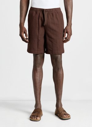 Homme portant un short marron jusqu'aux genoux avec un cordon de serrage, assorti à des sandales marron à bout ouvert et un haut blanc sans manches.
