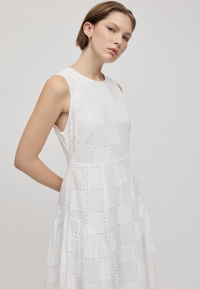 Abito bianco con un design testurizzato che presenta quadrati ritagliati e motivi circolari. Senza maniche, con un corpetto aderente e una gonna a ruota.