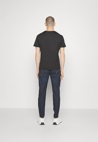 Czarna koszulka z krótkim rękawem w połączeniu z ciemnoniebieskimi dżinsami. Koszulka ma prosty design; dżinsy mają tylne kieszenie z tonowanym przeszyciem.