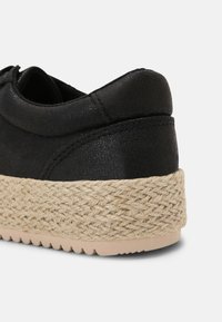 Černá teniska s texturovaným koženým svrškem a juty v espadrilovém stylu ve střední části podrážky. Měkká gumová podrážka se vzorem vln pro lepší přilnavost.