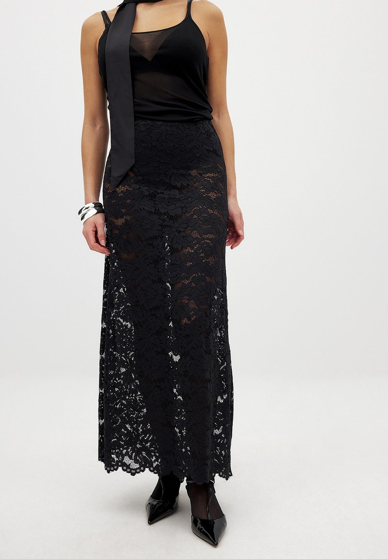Schwarzer Spitzen-Maxi-Rock mit eng anliegendem Bund und fließender Silhouette. Durchsichtige obere Schicht mit floralen Mustern, kombiniert mit einem schwarzen Satintop und Heels.