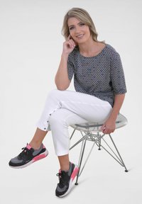 Geprinte zwart-witte top, witte cropped broek met knopen, zwart-roze sportschoenen, zittend op een transparante stoel.